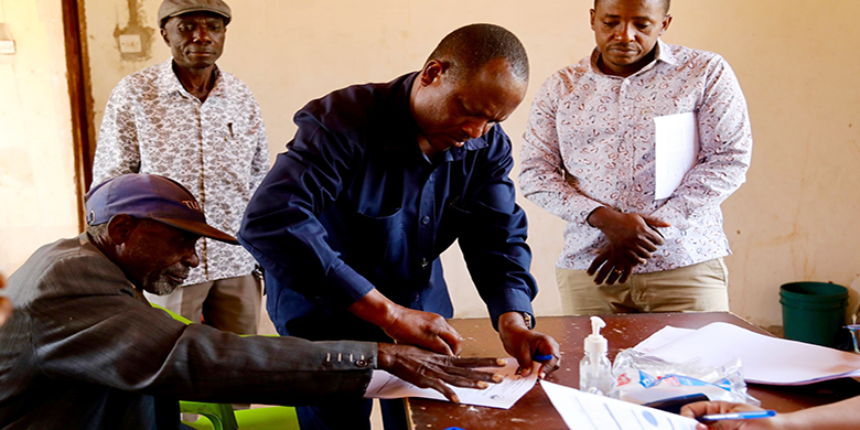 Afisa Mazingira kutoka Mamlaka ya Majisafi na Usafi wa Mazingira Dodoma (DUWASA), Ambrosi Siril akimsaidia mzee Peter Mazengo kusaini katika daftari la fidia katika eneo la Zuzu Nala jijini D