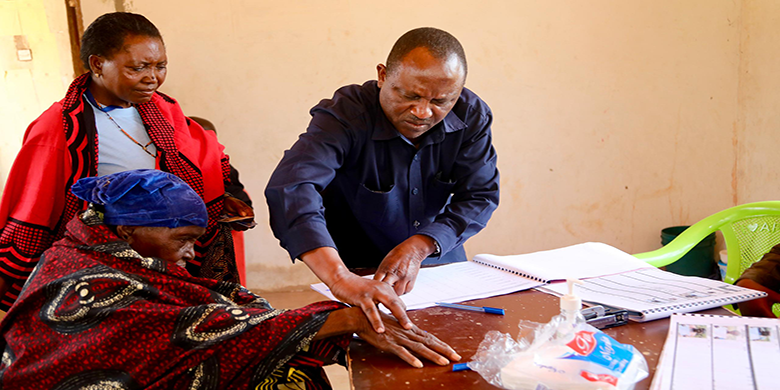 Afisa Mazingira kutoka Mamlaka ya Majisafi na Usafi wa Mazingira Dodoma (DUWASA), Ambrosi Siril akimsaidia Bibi Anna Masaka kusaini katika daftari la fidia katika eneo la Zuzu Nala jijini Dod
